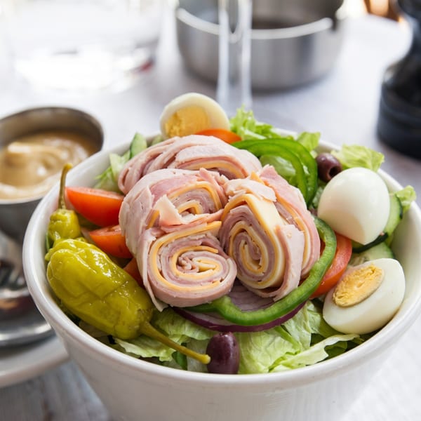 Chef salad with rolled ham and cheese, hard-boiled eggs, tomatoes, peppers, and olives.