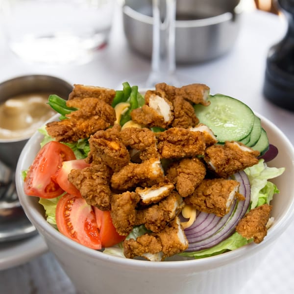 Crispy fried chicken pieces on a fresh salad with lettuce, tomatoes, cucumbers, and red onion.