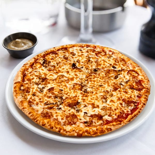 A whole mushroom pizza with melted cheese on a white plate, with a side of dipping sauce.